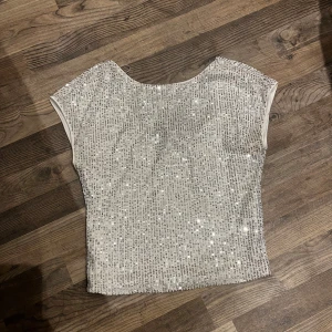 Glittrig topp från vero Moda  - Supersnygg glittrig topp från vero Moda i vitt med massor av silvriga paljetter. Modellen är ärmlös med rund halsringning och har en croppad passform. Perfekt för dig som vill sticka ut och glänsa lite extra. Andvänd en gång