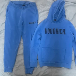 Blå tracksuit från Hoodrich - Säljer en snygg blå tracksuit från Hoodrich med stor logga på bröstet. Tröjan har en klassisk känguruficka och långa ärmar. Perfekt för en avslappnad stil. Matchande mjukisbyxor. Mycket bra skick knappt använd.