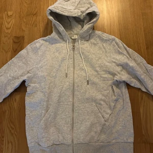 Grå hoodie med dragkedja - Säljer en bekväm grå hoodie med dragkedja och justerbar huva. Perfekt för avslappnade dagar. Den har långa ärmar och en klassisk passform. Ficka framtill för extra stil och funktionalitet.