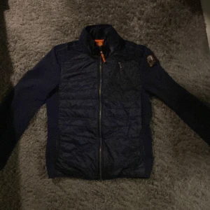 Mörkblå jacka från Parajumpers - Säljer en snygg mörkblå jacka från Parajumpers. Jackan har en dragkedja framtill och en liten bröstficka med dragkedja. Den har en broderad logga på ärmen och är perfekt för kyligare och varmare dagar. Knappt använd. Prutning vid snabb affär😁