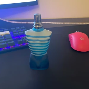Le Male Eau de Toilette från Jean Paul Gaultier ungefär 65-70 ml kvar - Ikonisk parfymflaska formad som en manlig torso med blå och turkosa ränder. Denna doft är känd för sin fräscha och sensuella karaktär, perfekt för den självsäkra mannen. Flaskan är både stilren och unik, vilket gör den till ett samlarobjekt.