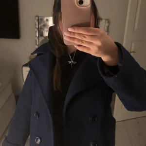 Mörkblå kappa från Design by si - Säljer en stilren mörkblå kappa från Design by Ri. Den har en klassisk dubbelknäppt design med stora knappar och två framfickor. Perfekt för kyligare dagar med sin eleganta look. Den är som sagt väl använd och lite nopprig🩷men väldigt fin💙