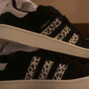 Svarta Adidas Campus med leopardmönster - Snygga svarta Adidas Campus sneakers med leopardmönstrade ränder. Perfekta för att ge din outfit en cool touch. Storlek 38 men passar även 37 och 39. Inte så mycket använda. KOM MED PRISFÖRSLAG! den med bäst pris får dom 