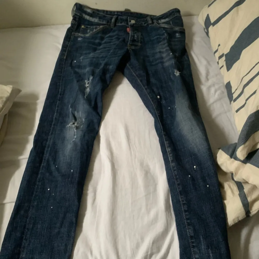 Snygga blå jeans från Dsquared2 med slitna detaljer och en klassisk femficksdesign. Jeansen har en knappgylf och en röd logotypetikett vid fickan. Perfekta för en avslappnad stil.. Farkut & Housut.