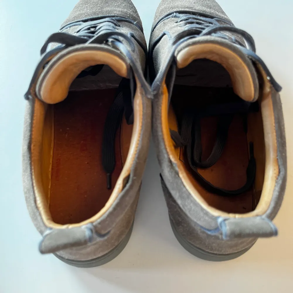 Snygga grå sneakers från Christian Louboutin med den ikoniska röda sulan. Skorna har snörning och är tillverkade i mocka, vilket ger en lyxig känsla. Perfekta för dig som vill ha en stilren och exklusiv look.. Kengät.