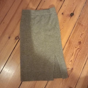 Grå stickad kjol från VILA - Snygg grå stickad kjol från VILA i storlek L. Kjolen har en ribbad kant och en diskret slits framtill som ger en stilren look. Perfekt för kyligare dagar. Ca 71cm lång och 73 i midjan (omkrets). Väldigt streshig och bekväm. Sticker inget alls. 