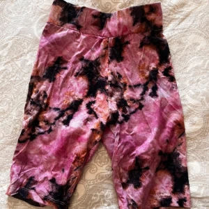 Färgglada cykelbyxor - Säljer ett par färgglada cykelbyxor med batikmönster i rosa och svart. De har en bekväm passform och är gjorda i ett mjukt material.
