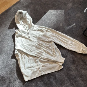 Vit zip-hoodie från Uniqlo - Säljer en stilren vit hoodie från Uniqlo. Den har en dragkedja framtill och en klassisk huva. Perfekt för en avslappnad look.