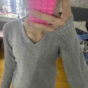 Grå stickad tröja - Säljer en mysig grå stickad tröja med v-ringning. Tröjan har långa ärmar och en enkel design som passar perfekt för kyligare dagar. Perfekt för lager-på-lager-stil eller att bära som den är.