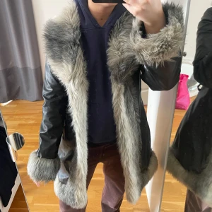 Svart kappa med fuskpäls  - Snygg och unik svart kappa från Only med grå fuskpälsdetaljer längs kragen, ärmsluten och framkanten. Storlek M