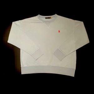 Blå sweatshirt från Ralph Lauren - Säljer en stilren blå sweatshirt från Ralph Lauren med det klassiska röda logotypbroderiet på bröstet. Tröjan har långa ärmar och ribbade muddar vid ärmslut och nederkant. Perfekt för en avslappnad look.