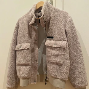 Beige teddyjacka från Didriksons - Mysig beige teddyjacka från Didriksons med dragkedja och knappar framtill. Jackan har två stora fickor med lock och en hög krage för extra värme. Perfekt för kyliga dagar! Storlek 170 men skulle säga att den passar mig som vanligtvis har storlek S. Säljs på flera sidor. 