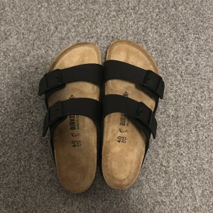Svarta Birkenstock - Säljer ett par klassiska svarta Birkenstock med två justerbara remmar och en bekväm korksula. Perfekta för en avslappnad stil och komfort hela dagen. Sulan har ett mönster för extra grepp. Aldrig använda pga inte passat mig. Kan gå ner vid snabb affär 