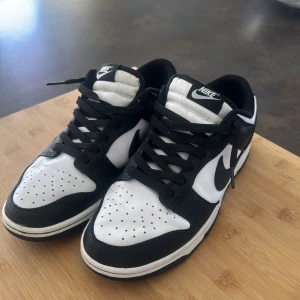 Svartvita Nike Dunk sneakers - Snygga svartvita Nike Dunk sneakers med klassisk design. Skorna har en låg profil och är tillverkade i syntetmaterial med snörning framtill. Perfekta för en stilren look.