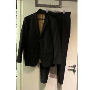 Svart Esprit kostym med kavaj och byxor - Säljer en klassisk svart kostym med kavaj och matchande byxor. 