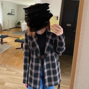 Rutig kavaj i svart och beige - Snygg rutig kavaj i svart och beige med dubbelknäppning. Perfekt för en stilren look. Kavajen har långa ärmar och en klassisk krage.