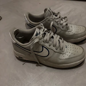  Nike Air forces - Säljer ett par klassiska vita Nike Air forces med blå detaljer. Skorna har snörning och en perforerad tå för extra ventilation. Perfekta för en sportig och stilren look.