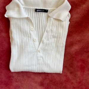 Vit ribbad pikétröja från Gina Tricot - Säljer en stilren vit ribbad pikétröja från Gina Tricot. Tröjan har en klassisk krage och knappar framtill. Perfekt för en avslappnad men ändå snygg look. Passar bra till både jeans och kjol. Endast använd en gång, sen blev den för liten för mig och min gravida mage! 