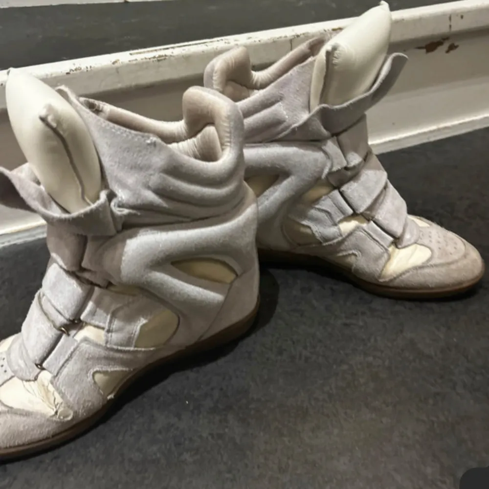 Snygga beige sneakers med kilklack och flera kardborreband. Skorna har en unik design med vadderade detaljer och perforerad tå. Perfekta för en trendig look. Lite defekter vid sidan av skorna där det har creasat. Har ej kvitto men dust bag tillkommer! (Priset är ej hugget i sten, går att pruta vid snabbt köp!). Kengät.