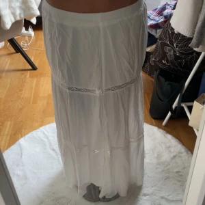 Vit långkjol med spetsdetaljer - Säljer en vacker vit långkjol med fina spetsdetaljer. Kjolen är tunn och lite genomskinlig. Den är även inte tajt med en stretchig midja. 
