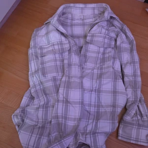 Rutig skjorta i beige och vit - Säljer en stilren rutig skjorta i beige och vit. Skjortan har långa ärmar och två bröstfickor med lock. Perfekt för en avslappnad look.