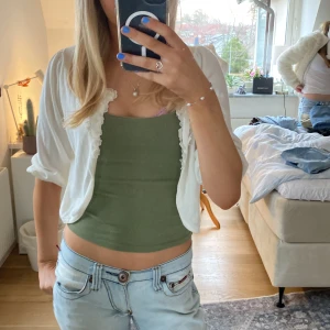 Vit bolerotopp med blommig spetsdetalj - Säljer en söt vit bolerotopp med vackra blommiga spetsdetaljer längs kanten. Toppen har trekvartsärmar och är perfekt för att lägga till en romantisk touch till din outfit. Passar bra över en enkel topp eller klänning.