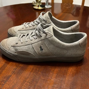 Grå sneakers från Polo Ralph Lauren - Snygga grå sneakers från Polo Ralph Lauren med klassisk design och snörning. Skorna har en diskret logotyp på sidan och är tillverkade i mocka för en stilren look. Perfekta för en avslappnad stil. Nypris:1199