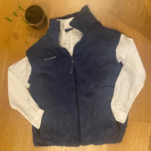 Blå fleeceväst från Columbia - Säljer en blå fleeceväst från Columbia med dragkedja framtill. Västen har en hög krage och är perfekt för lager-på-lager under kyligare dagar. Den är stilren och funktionell med två praktiska fickor med dragkedja. Storlek L, men passar M. Jättebra skick och en perfekt fleece väst till våren.