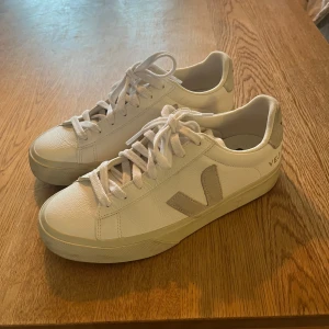 Vita sneakers från Veja - Snygga vita sneakers från Veja med klassisk design och snörning. Skorna har en diskret logga på sidan och baksidan. Perfekta för en stilren look. Använda ett fåtal gånger så i mycket fint skick! Nypris 1650kr