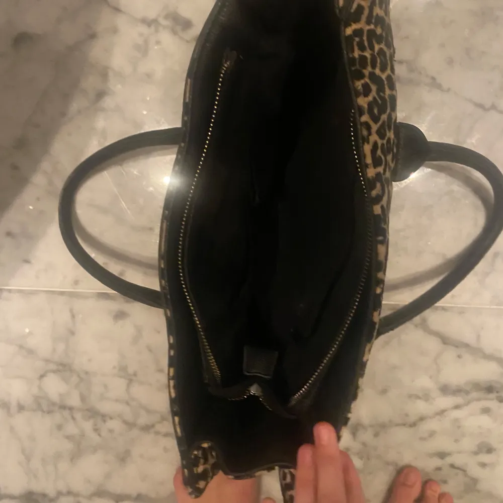 Säljer en snygg leopardmönstrad handväska med svarta handtag och detaljer. Väskan har en dragkedja och ett stilrent spänne framtill. Perfekt för att ge din outfit en djärv touch! 🐆🖤. Laukut & Käsilaukut.