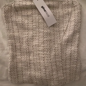 Vit tubtopp från Gina Tricot - Säljer en stilren vit tubtopp från Gina Tricot. Toppen har ett diskret rutmönster och är perfekt för att skapa en chic look. För liten för mig