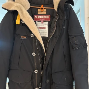 Svart parkajacka från Parajumpers - Säljer en svart parkajacka från Parajumpers med snygga detaljer som knappar och dragkedja. Jackan har en mysig fodrad huva och flera praktiska fickor. Perfekt för kalla dagar med sin robusta design och varma material. Den användes endast 1 vinter och köptes från Johnells för 12 500kr, säljes endast för 5000 kr, den är i mkt gott skick och storlek S, pris kan diskuteras vid snabb affär 