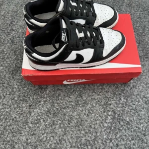 Svartvita Nike sneakers - Snygga svartvita Nike sneakers med klassisk design. Skorna har snörning och perforerade detaljer på ovansidan för extra stil. Perfekta för en casual look. Original box tillkommer. Storlek 40.5. Hör av dig vid frågor eller funderingar ✅