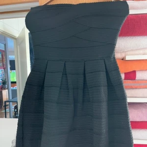 Svart axelbandslös klänning från Pimkie - Snygg svart axelbandslös klänning från Pimkie med dragkedja i ryggen. Klänningen har en strukturerad yta och en kort längd som ger en elegant look. Perfekt för en kväll ute eller en speciell tillställning.