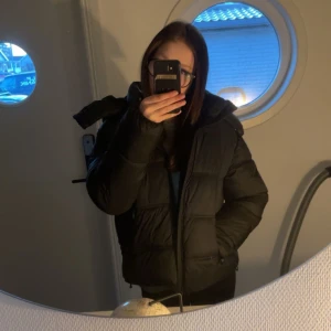 Svart pufferjacka - Säljer en svart pufferjacka med lång ärm och dragkedja. Jackan är perfekt för kyligare väder och har en mysig, vadderad design som håller dig varm. Den har en klassisk look och passar bra till vardags.