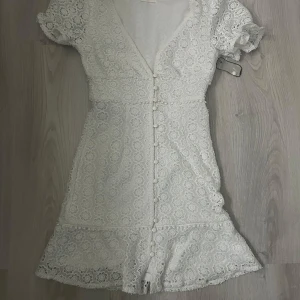 Vit spetsklänning från Kiss The Sky - Säljer en söt vit spetsklänning från Kiss The Sky i storlek XS. Klänningen har korta puff ärmar och en v-ringad design med knappar framtill. Perfekt till studenten!🌸volang ner till,vill man inte ha lika stor v ringning så tillkommer det en till knapp man kan sy på!(bild 5)