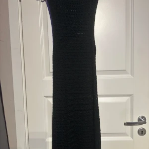 Svart stickad långklänning - Snygg svart stickad långklänning med ett enkelt och stilrent mönster. Perfekt för en elegant look. Klänningen har en rund hals och är ärmlös, vilket gör den både bekväm och chic.