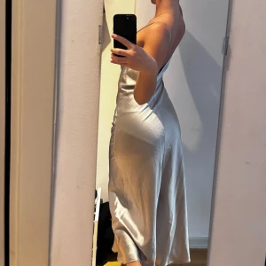 Champagnefärgad sidenklänning - Elegant champagnefärgad klänning i siden med smala axelband och v-ringad hals. Klänningen har en smickrande passform och faller vackert längs kroppen. Perfekt för speciella tillfällen.