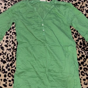 Grön klänning med knappar - Säljer en grön klänning med trekvartsärm och knappar framtill. Klänningen har en avslappnad passform och är perfekt för vår och sommar. Den är tillverkad i ett lätt och bekvämt material.