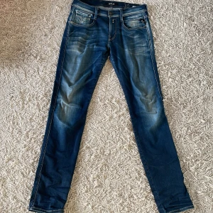 Blå jeans Replay Anbass - Snygga blå jeans från Replay med en klassisk femficksdesign och lätt slitna detaljer. De har en normal passform och är perfekta för en avslappnad stil. Märkeslappen på baksidan ger en autentisk touch.