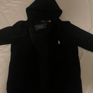  Polo Ralph Lauren hoodie - Säljer en stilren svart hoodie från Polo Ralph Lauren med den klassiska loggan på bröstet. Perfekt för en avslappnad look. Hoodien har långa ärmar och en bekväm passform. Den är M funkar också som S. Den är helt nytt skick inte använt en enda gång. Tveka ej på att fråga frågor👋