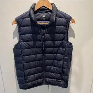 Svart dunväst från Uniqlo - Ultra light down täckväst från Uniqlo i mycket  bra skick. Drajkedja fram och dolda fickor i sidorna med dragkedja. Storlek XS.  Marinblå, både på utsidan och insidan. (Sålt en annan väst precis i storlek S varav två annonser).