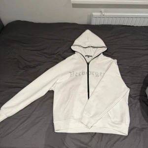 Verborgen vit hoodie - Denna vita hoodien i storlek M har en unik design med rhinestones och en dragkedja som går ända upp till toppen av luvan, materialet på hoodien är bomull och polyester. Ny pris på tröjan är 1300kr.