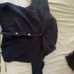 Mörkblå kortärmad tröja med knappar - Snygg mörkblå tröja med korta ärmar och klassisk krage. Tröjan har raka linjer, knäppning framtill med ljusa knappar och är tillverkad i ett mjukt, stickat material som känns skönt mot huden. Perfekt för dig som gillar en chill och stilren look. Man kan även använda tröjan till en kofta. Aldrig använt så inget fel på den.