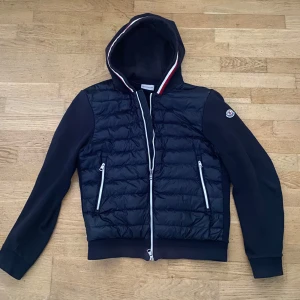 Moncler cardigan - Mörkblå cardigan från Moncler med quiltad front, vita dragkedjor och huva med röd, vit och blå kant.  Pris kan diskuteras, äkta