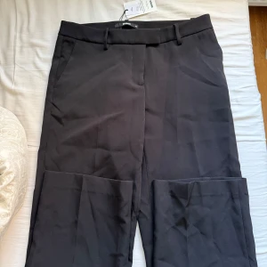 Svarta kostymbyxor från bikbok  - Snygga svarta kostymbyxor från bikbok med klassisk rak passform och hällor för bälte. Byxorna har diskreta sidfickor och är perfekta för en clean och stilren look. Materialet känns mjukt och har en lätt stretch. Oanvända med prislappen kvar