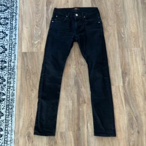 Lee Luke skinny W29 L32 - Snygga svarta jeans från Lee med klassisk femficksdesign. Jeansen har smal passform och raka ben, tillverkade i stretchig denim. Kameran får närbilderna på byxorna att se gråa ut men de är helt svarta som på helbilderna. Såklart tvättade innan dem skickas.