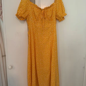 Gul prickig midiklänning med puffärm - milkmaid modell  - Superfin gul midiklänning med vita prickar och puffiga korta ärmar. Klänningen har söt knytning vid bysten, smock i ryggen och volangdetaljer vid ärmslut. Perfekt för sommarens alla tillfällen och ger en riktigt glad vibe!