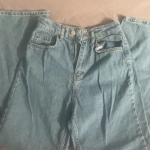 Ljusblå raka jeans med hög midja - Säljer ett par klassiska ljusblå jeans med raka ben och hög midja. Jeansen har fem fickor, dragkedja och knapp framtill samt snygga kontrastsömmar. Perfekta för en chill och tidlös look.