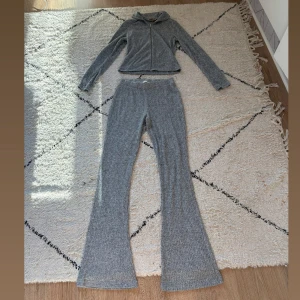 Grå ribbade mjukisbyxor från Lager 157 - Mysiga grå ribbade mjukisbyxor från Lager 157 i storlek XS. Byxorna har bootcut-ben och är tillverkade i ett mjukt, stickat material som är perfekt för chill dagar. Säljs tillsammans med matchande zip-hoodie om du vill ha ett komplett set.